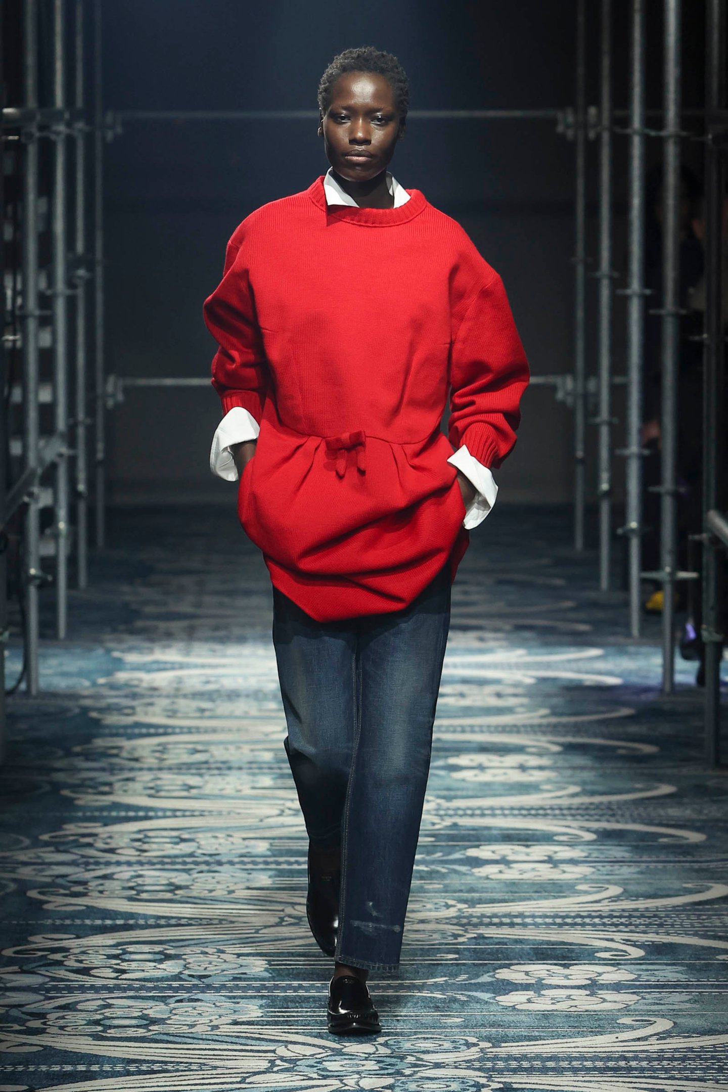 Modelo desfila com suéter tomato red e calça jeans, criando contraste marcante na passarela.