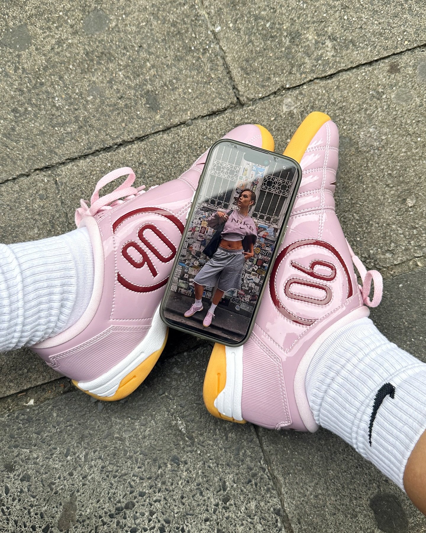 Tênis rosa com o número 90, com celular mostrando pessoa em roupa esportiva.