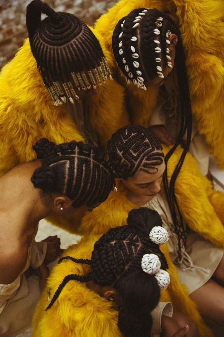 Pessoas com tranças elaboradas e contas, vestindo casacos amarelos. Estilo comum em salões afro.