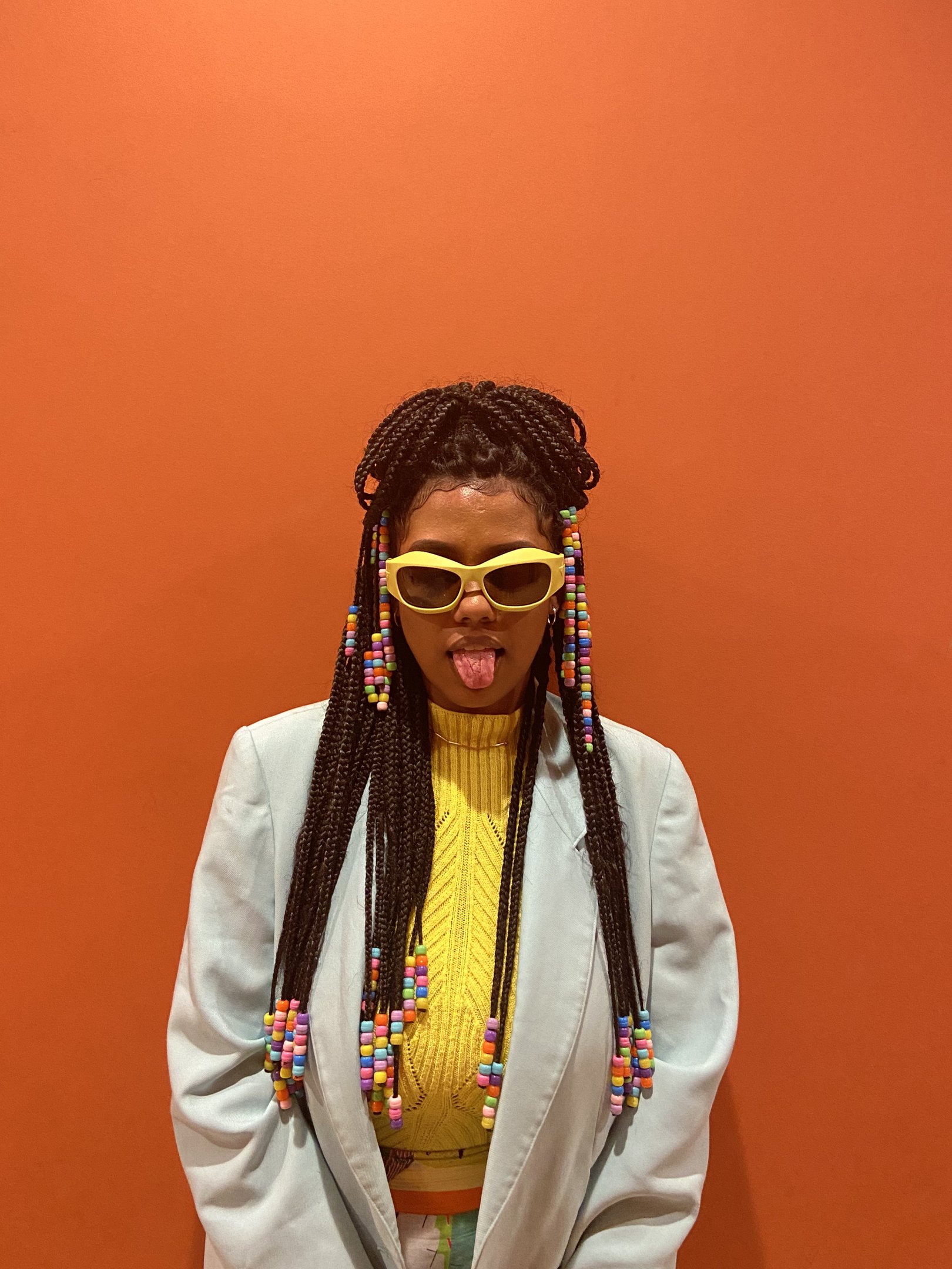 Trança com miçangas coloridas em fundo laranja, estilo comum em salões afro.