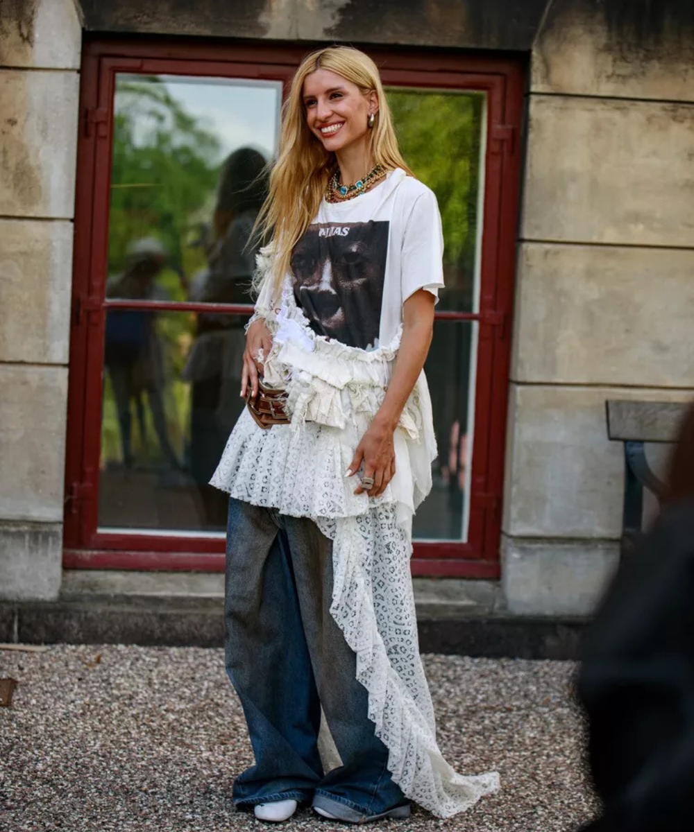 Pessoa com blusa estampada, sobreposição rendada, calça jeans larga e colar colorido.