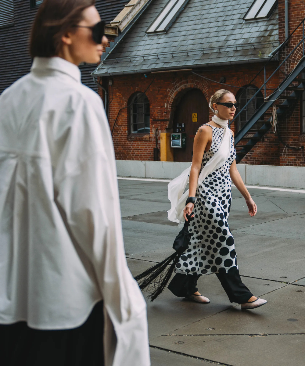Pessoa usando vestido de bolinhas sobre calça preta, andando em área urbana.