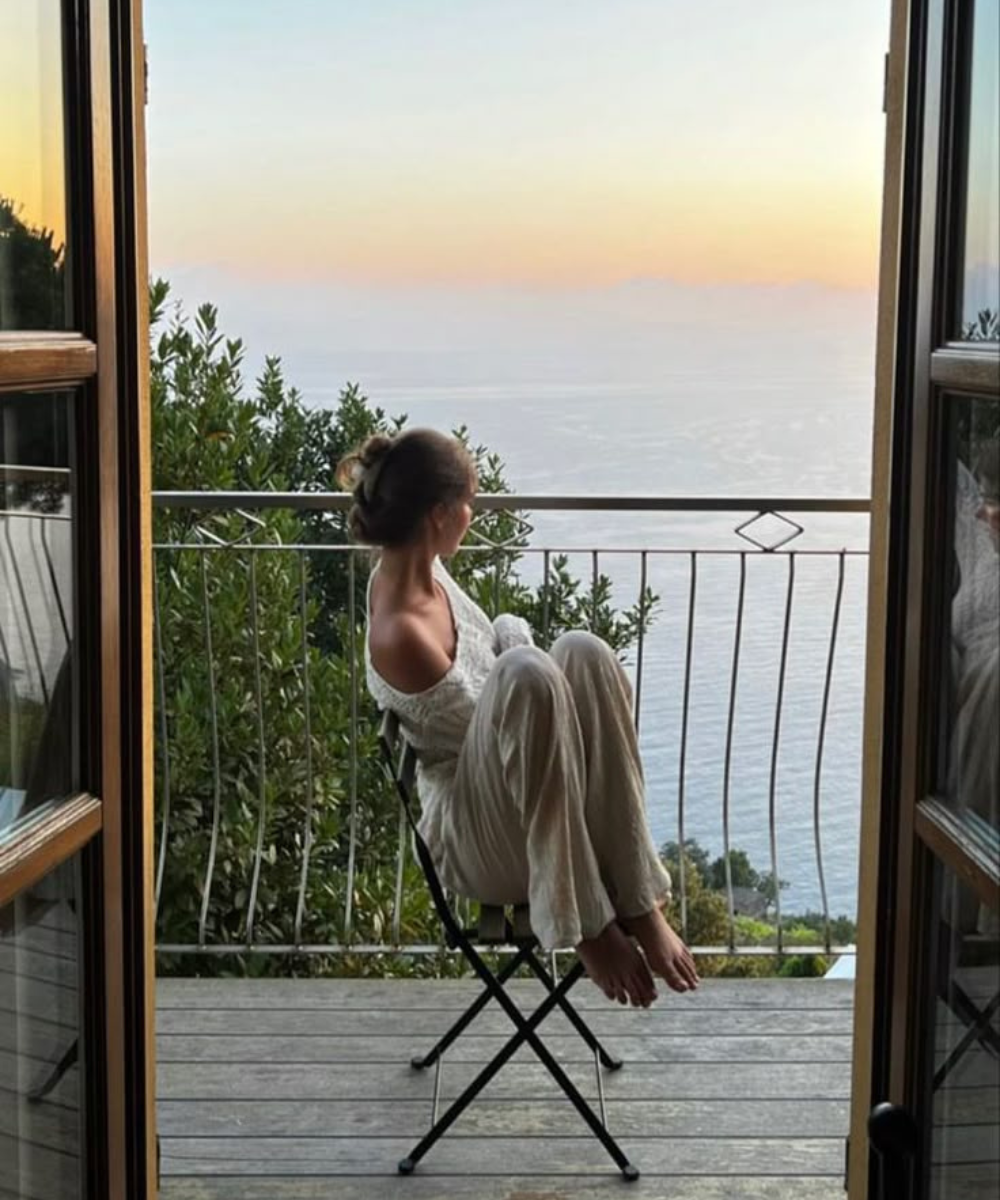 Pessoa sentada em uma varanda, apreciando o pôr do sol sobre o mar, simbolizando tranquilidade na vida adulta.