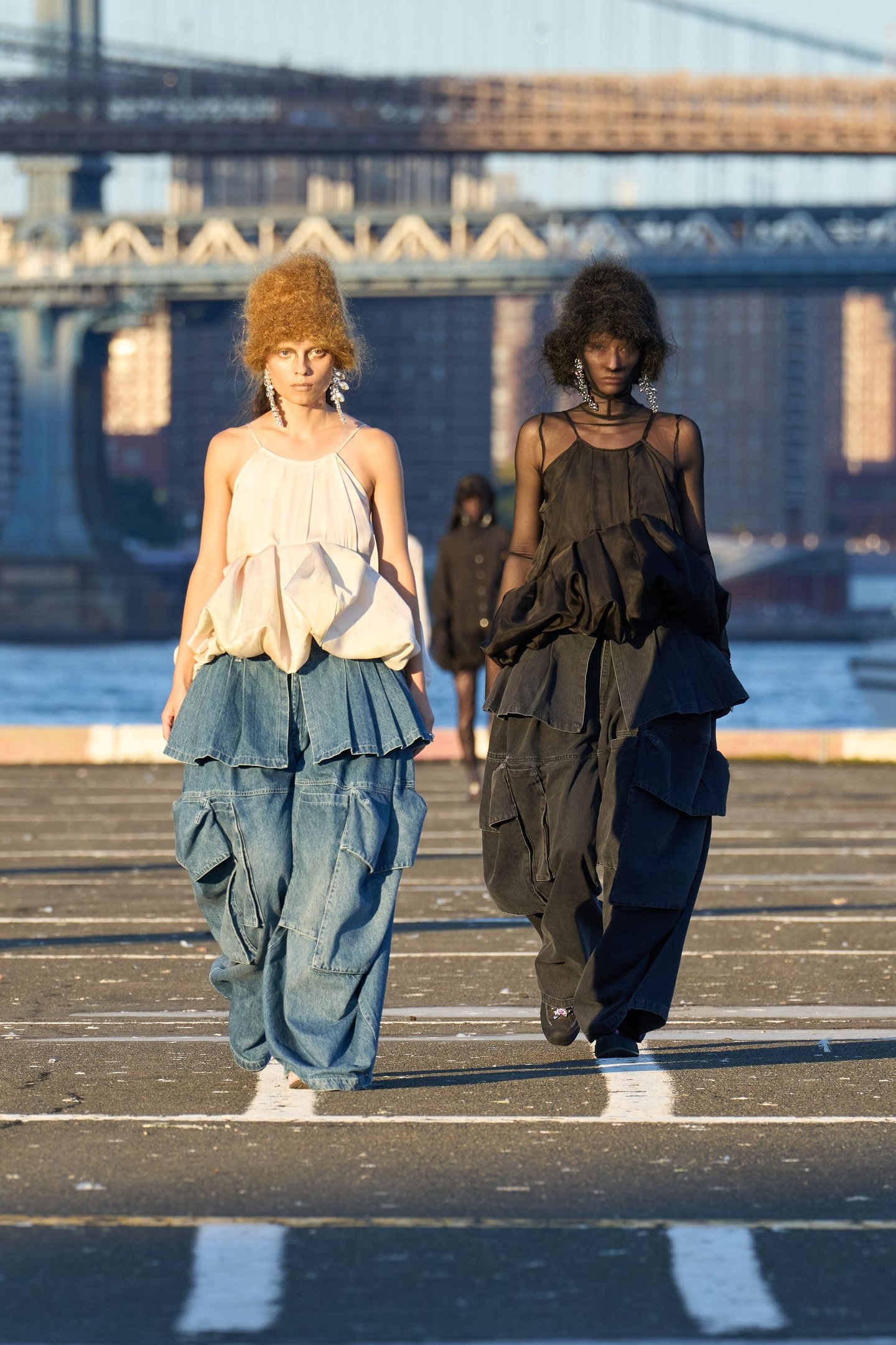 Modelos desfilando com looks volumosos e cabelo estilizado em uma passarela ao ar livre. New York Fashion Week SS26.