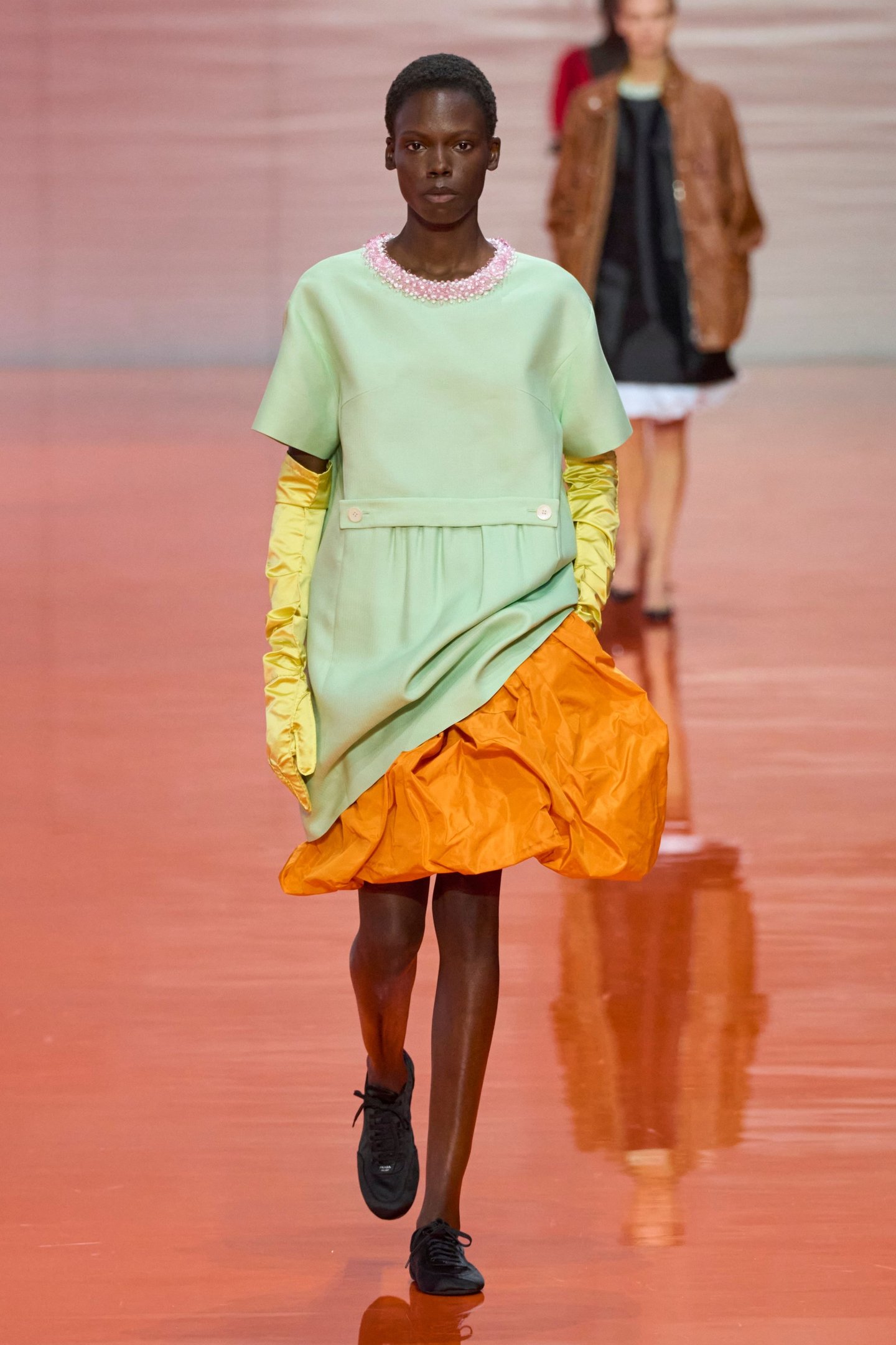 Modelo desfila com vestido verde claro e saia laranja na Milan Fashion Week SS26.