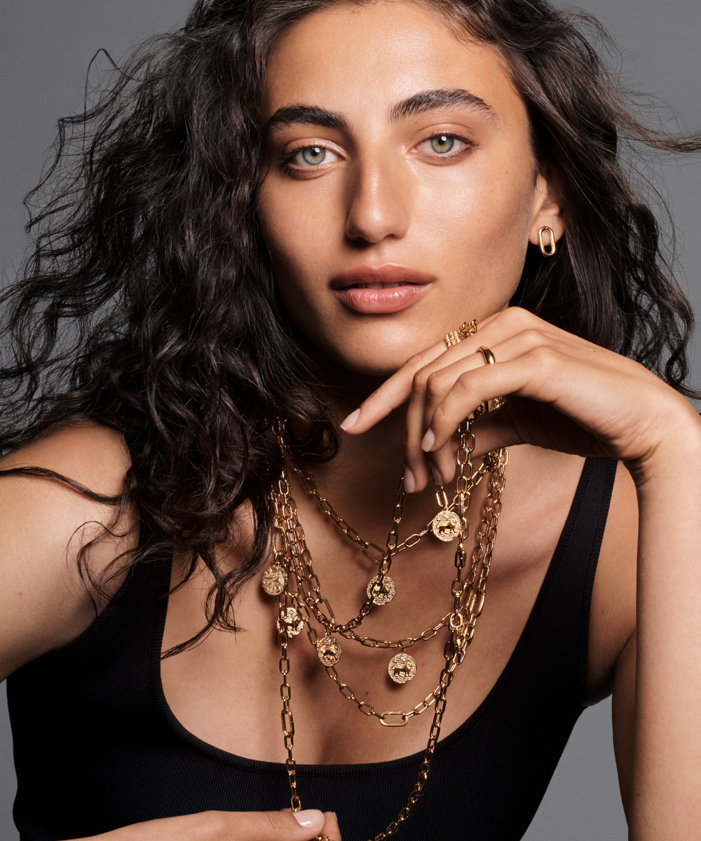 Uma mulher usa colares e anéis dourados, com destaque para o Pandora Talisman.