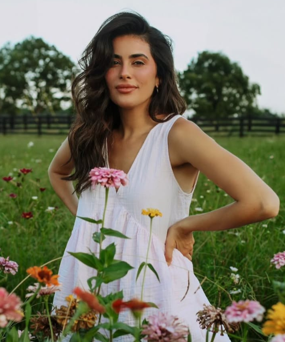 Pessoa de vestido branco posa em jardim florido, transmitindo vitalidade e saúde capilar, lembrando o melhor shampoo para queda de cabelo.