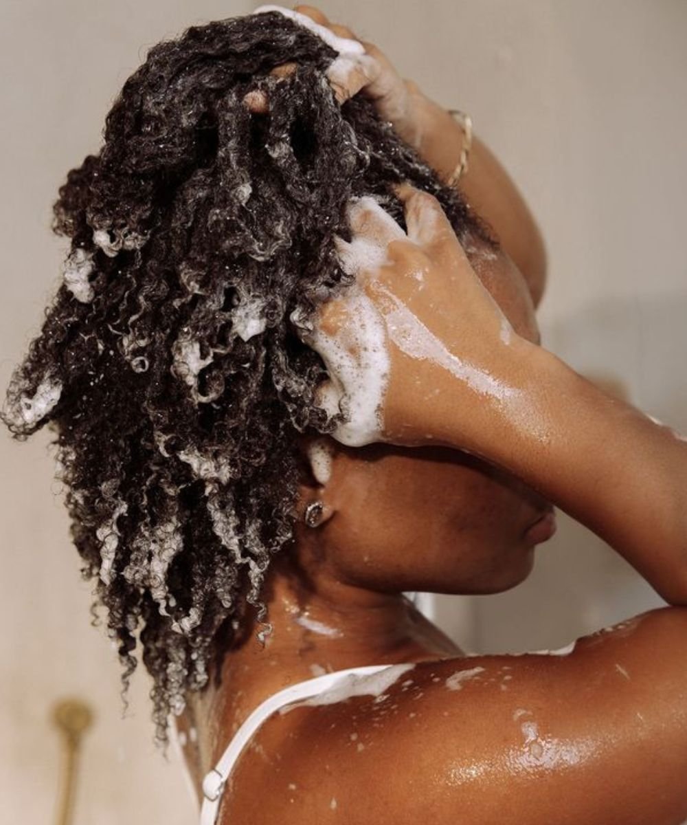 Cabelos cacheados sendo lavados com espuma abundante, destacando um momento de cuidado pessoal e uso do melhor shampoo.