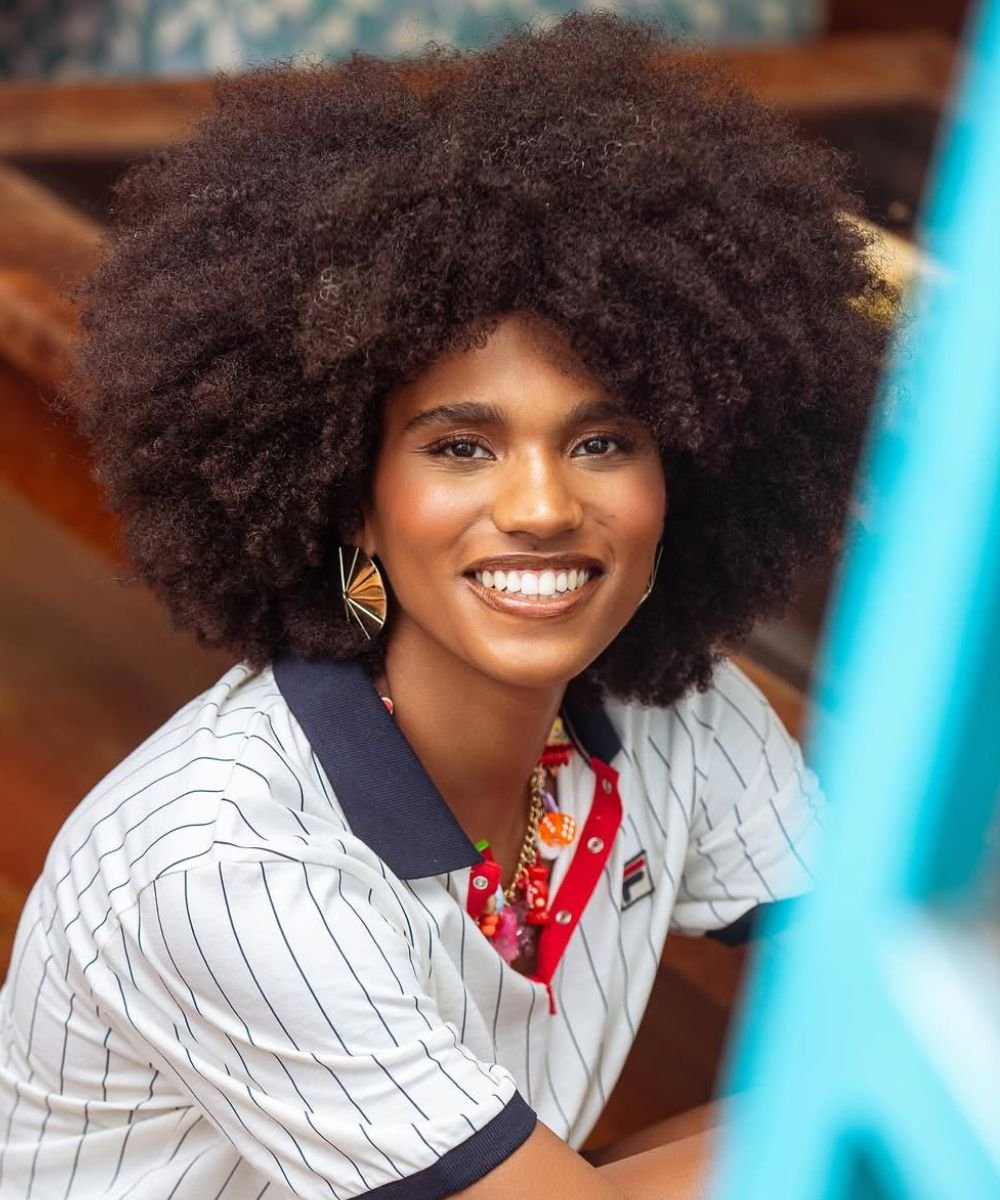 Mulher sorridente com cabelo volumoso em estilo afro, valorizando sua beleza natural depois de usar o melhor shampoo para ela.