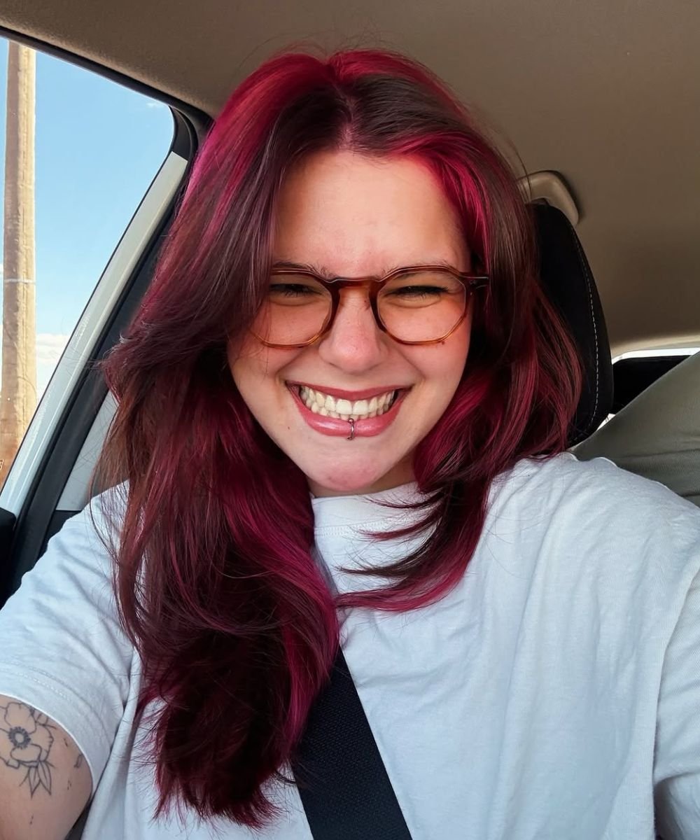 Pessoa sorridente com cabelo tingido de vermelho sentada no carro, transmitindo alegria e estilo, ressaltando um cabelo bem cuidado.