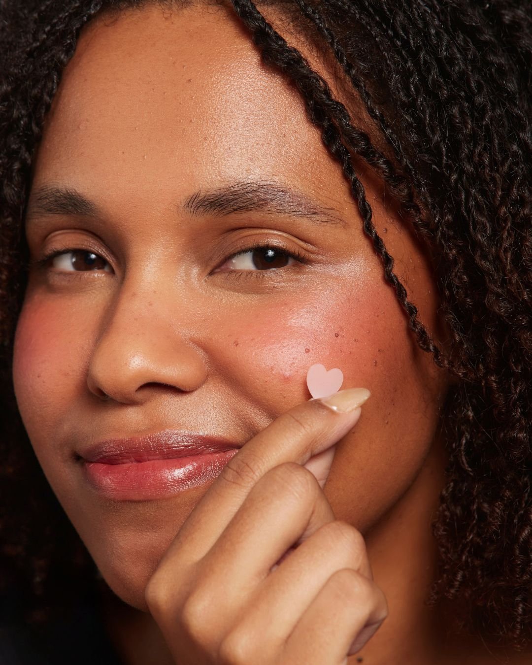 Jovem aplicando adesivo em formato de coração no rosto, relacionado ao cuidado com acne adulta.