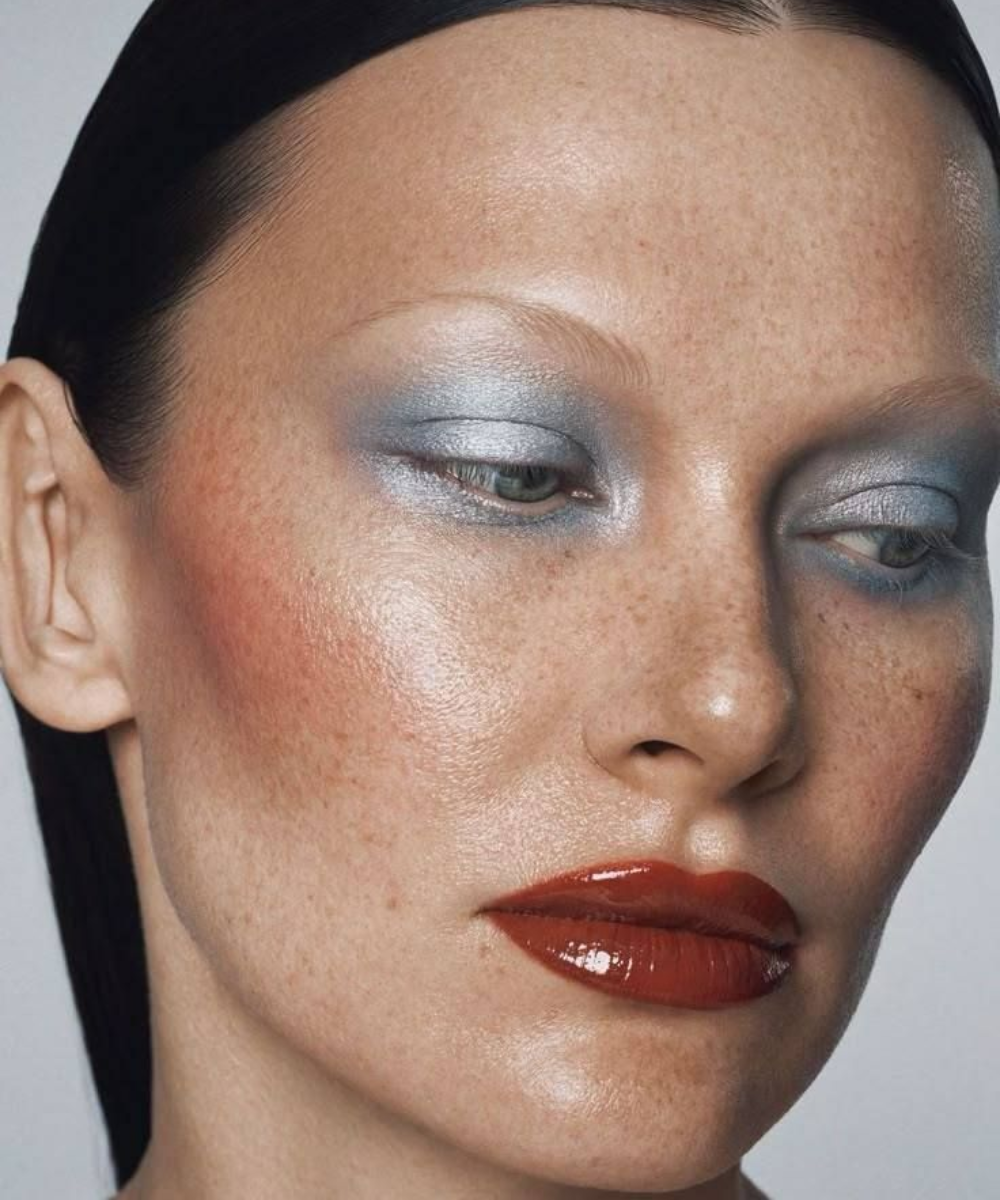 Mulher com maquiagem marcante, sombra azul e lábios vermelhos. Não é possível integrar a palavra 