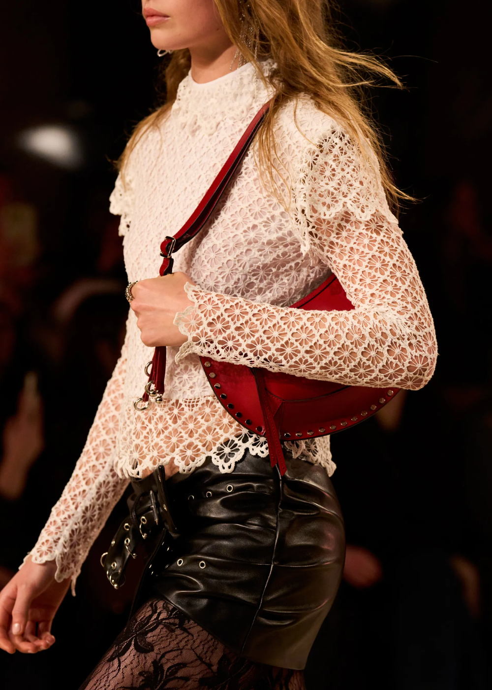 Mulher usando blusa de renda branca, saia de couro e bolsa vermelha com detalhes metálicos.