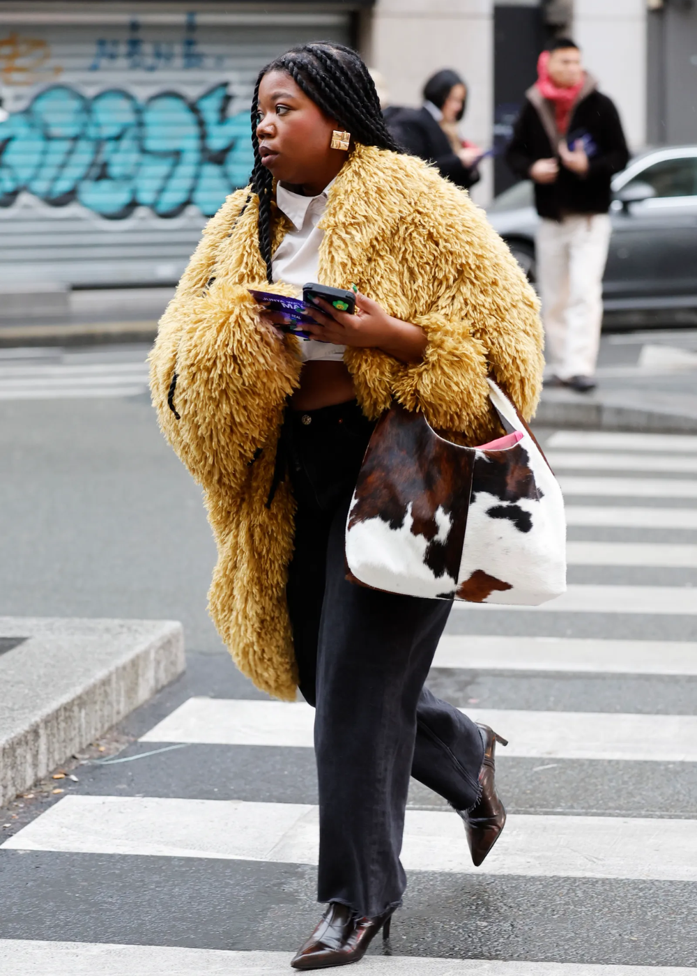 Mulher com casaco felpudo carrega bolsa com estampa estilosa de vaquinha enquanto atravessa a rua.