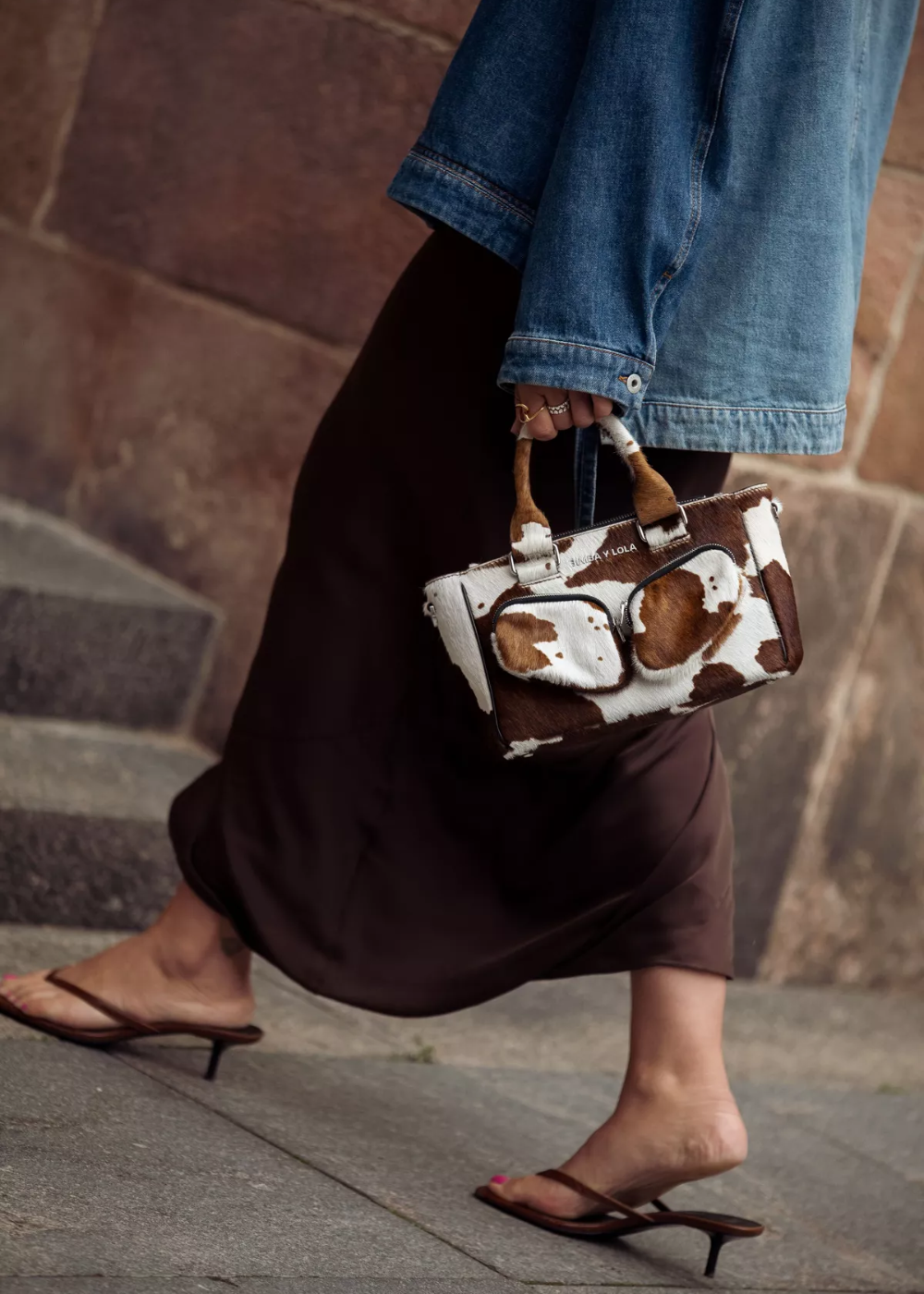 Bolsa com estampa estilosa de manchas, carregada por pessoa usando jaqueta jeans e sandálias.
