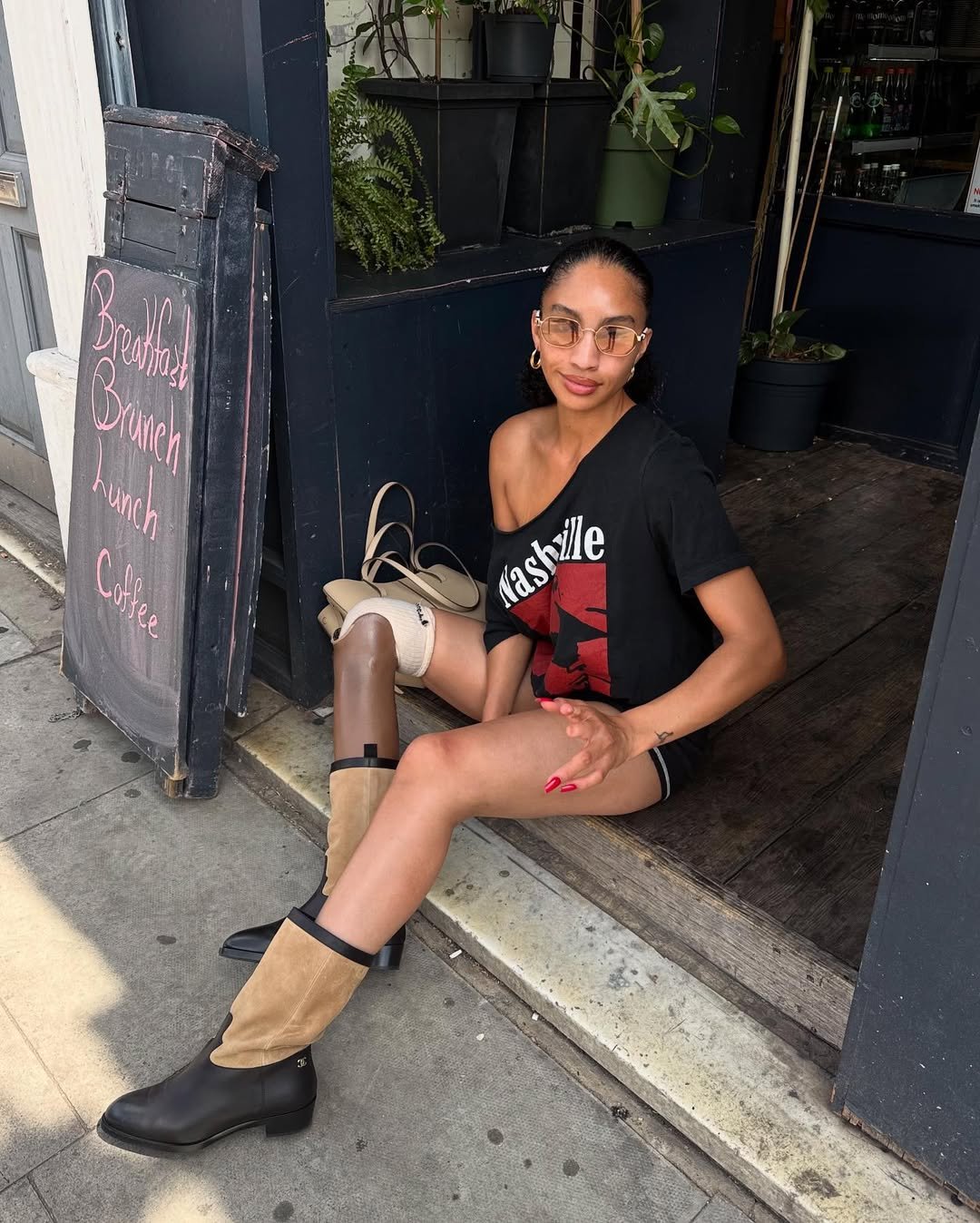 Pessoa usando camiseta com ombro caído, sentado em frente a um café, próximo a uma lousa com ofertas de brunch.