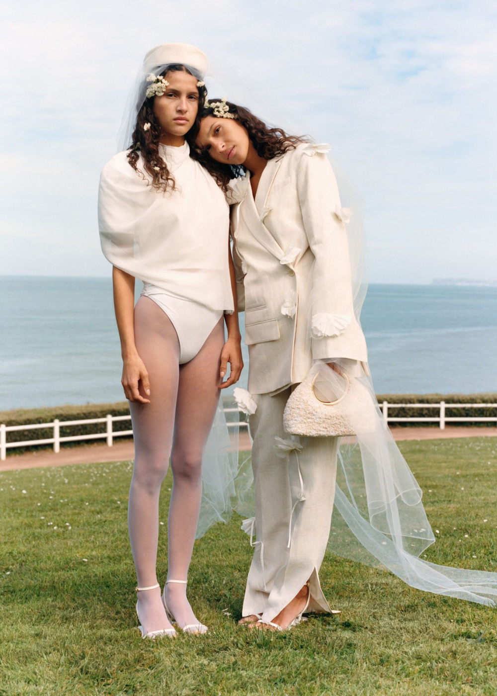 Duas mulheres em trajes de casamento alternativos posam em frente ao mar.