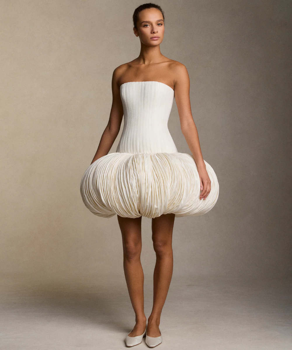 Modelo usando vestido não tradicional, volumoso na parte inferior e sem alças, em fundo neutro.