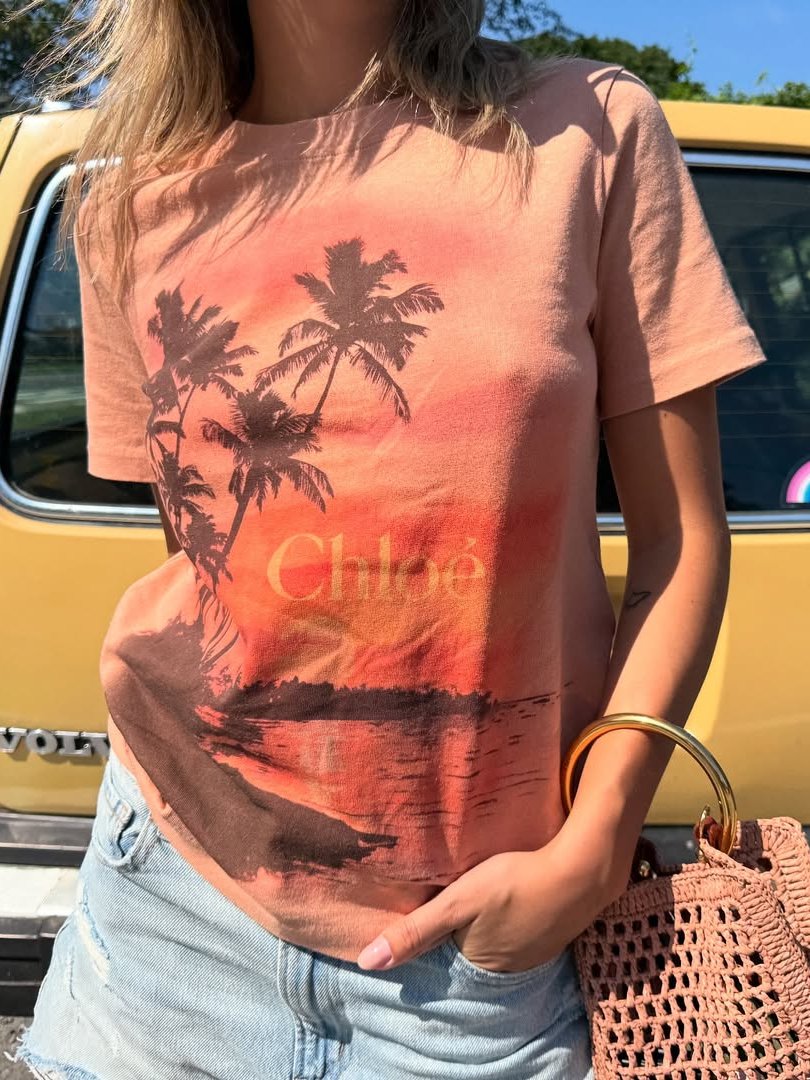 Graphic tee com estampa de palmeiras ao pôr do sol, jeans desfiado e bolsa de crochê. fundo carro amarelo.