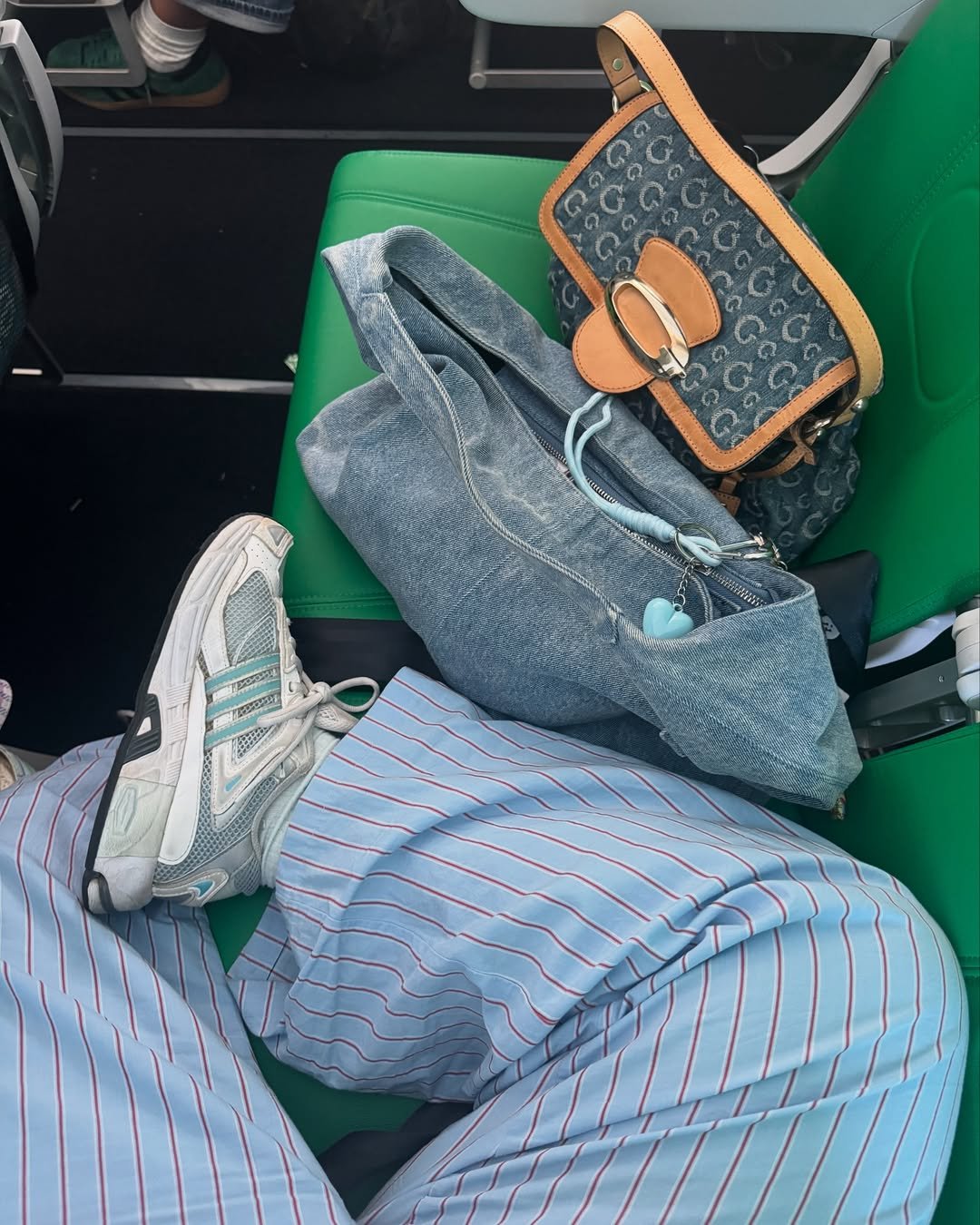 Chunky sneaker ao lado de bolsas e calça listrada azul em assento verde.