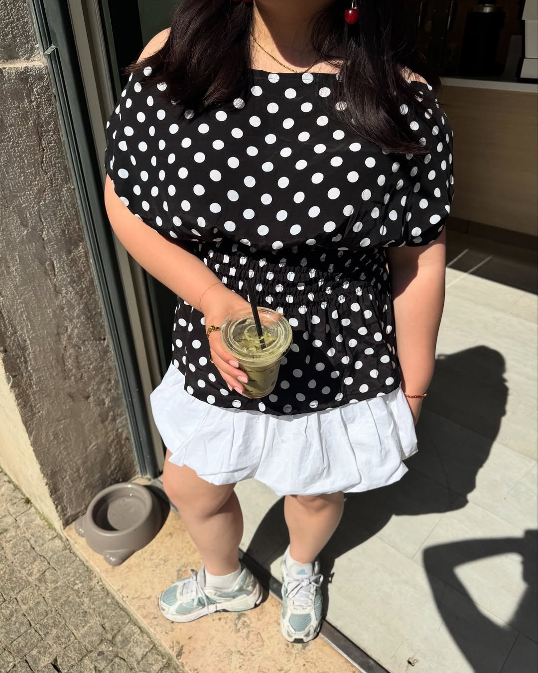 Pessoa usando vestido de bolinhas, segurando bebida, calçando chunky sneaker azul e branco.