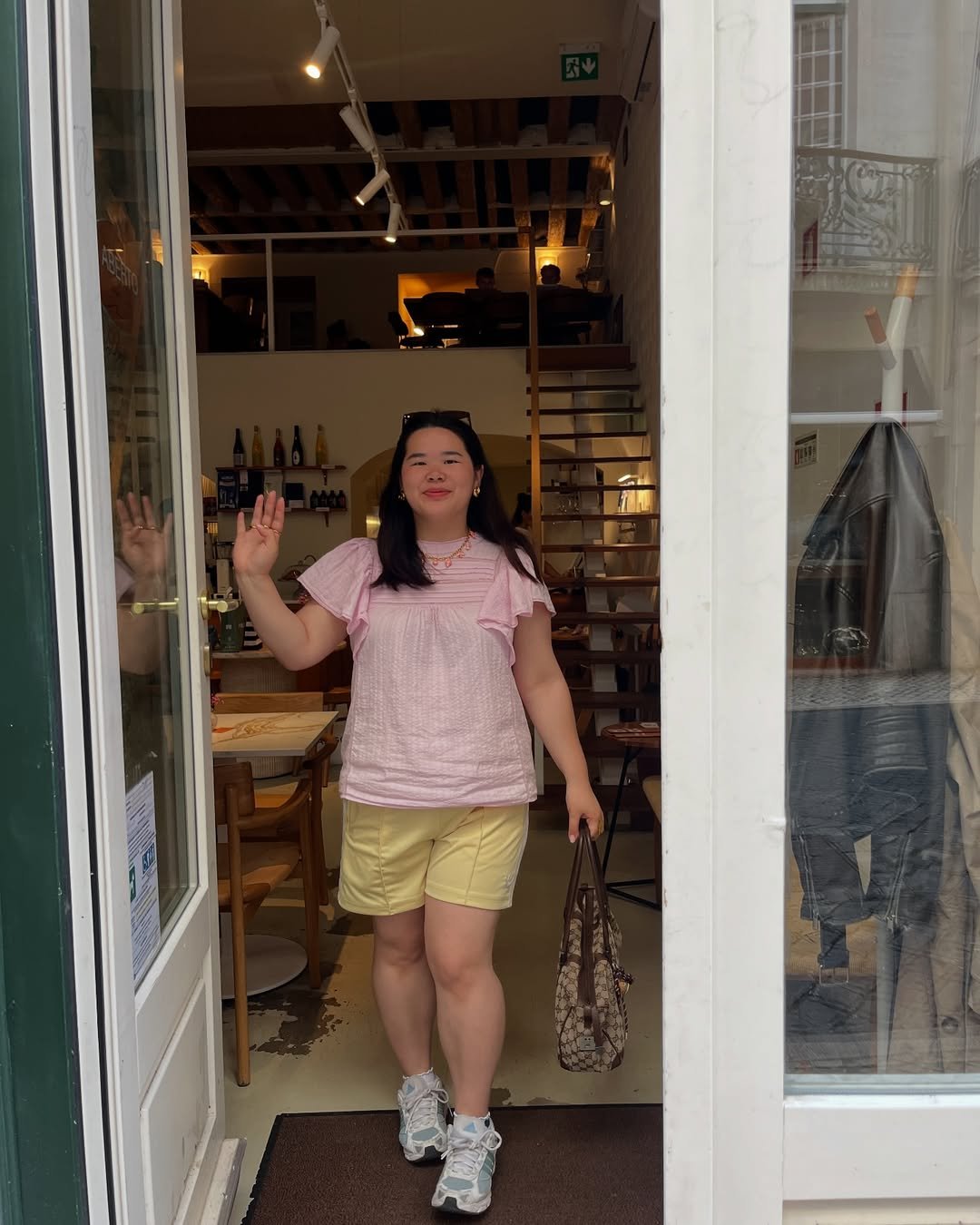 Pessoa saindo de uma loja, vestindo blusa rosa, shorts amarelo e carregando uma bolsa. Usa chunky sneaker branco.