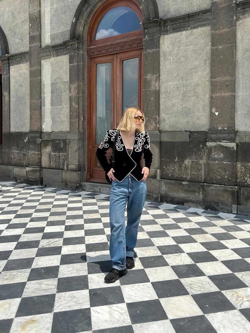 Pessoa de óculos escuros em pátio xadrez, com palácio histórico ao fundo, na Cidade do México.