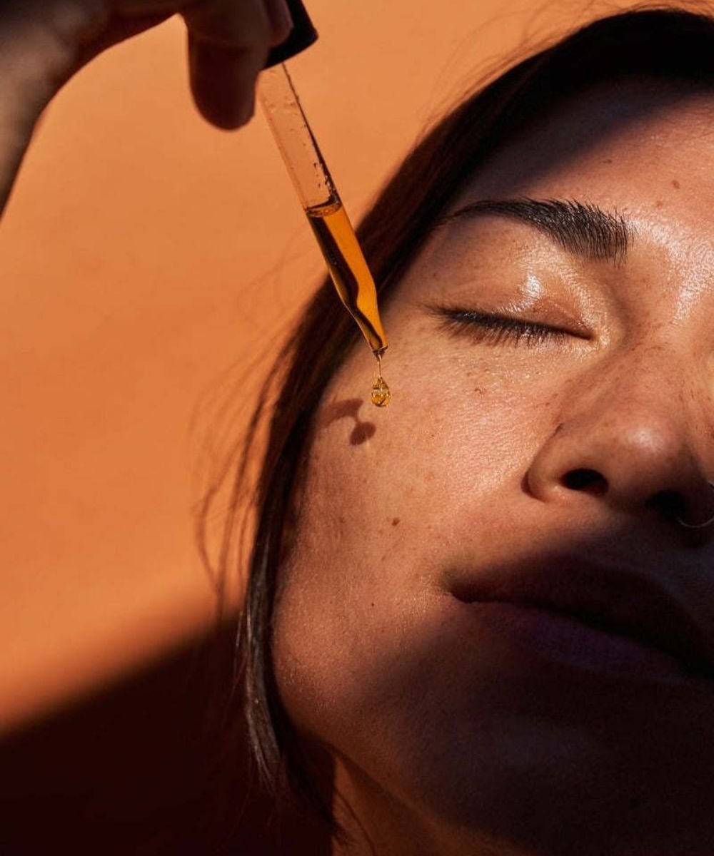Pessoa aplica sérum facial com conta-gotas em pele iluminada pelo sol para acabar com os cravos.