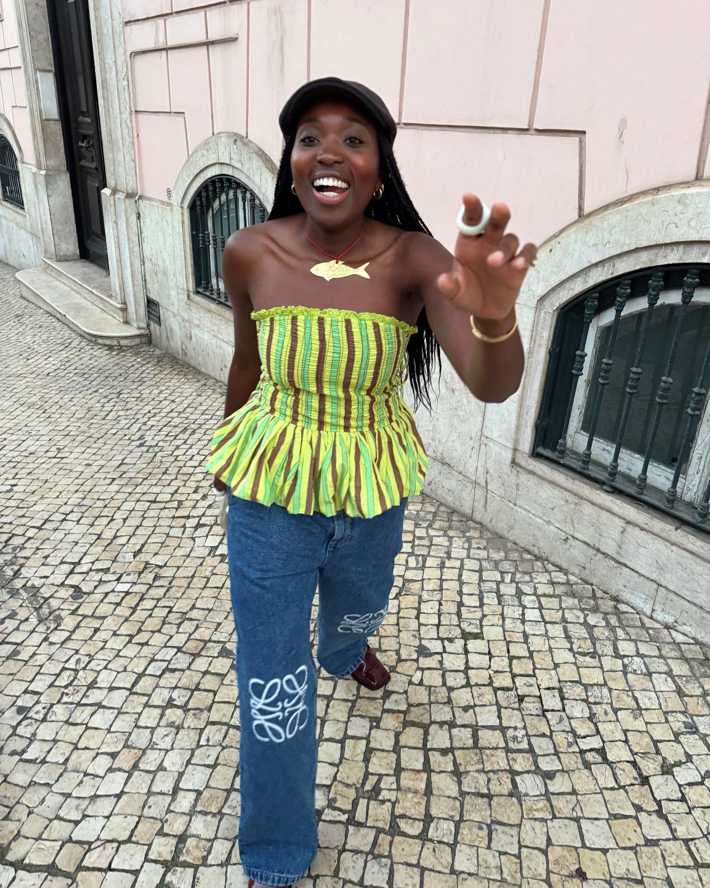 Pessoa sorrindo na rua com blusa peplum listrada e calça jeans estampada.