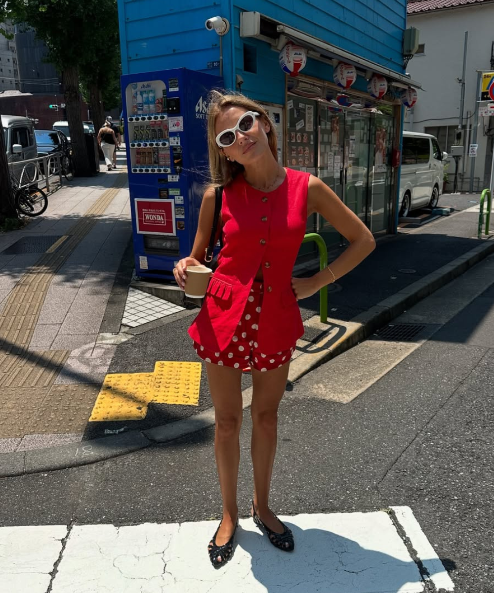 Pessoa usando shorts de poá vermelho e branco, colete vermelho e óculos de sol, segurando um copo. Mostra como usar poá na primavera.