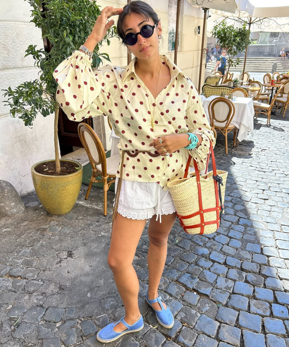 Blusa de poá combina com bermuda branca, sapatos azuis e bolsa de palha, ideal para a primavera.