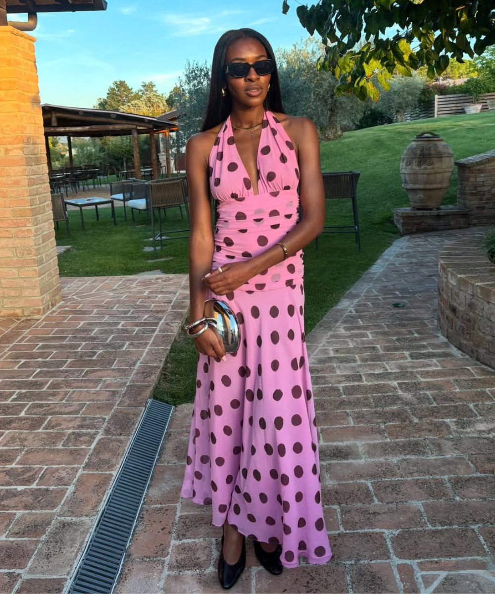 Vestido rosa com estampa de poá marrom, ideal para usar na primavera. Mulher segura uma clutch prateada.