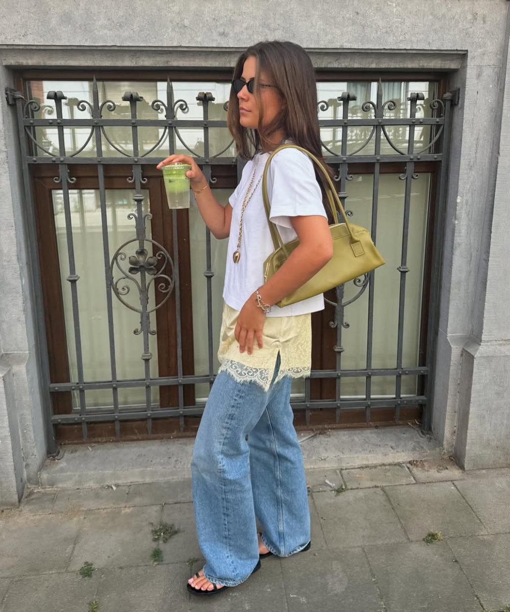 Pessoa com camiseta branca e calça jeans, adiciona um toque de renda ao look com sobreposição, segurando bebida.