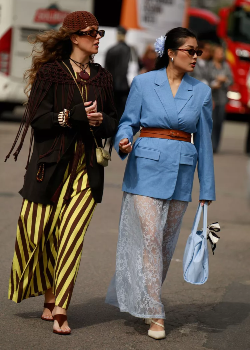 Duas mulheres caminham. Uma usa vestido azul com calça de renda, mostrando como usar renda no look.