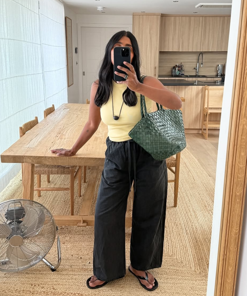 Pessoa com blusa amarela e calça preta segura bolsa verde, uma das cores de bolsa do verão, em sala decorada.