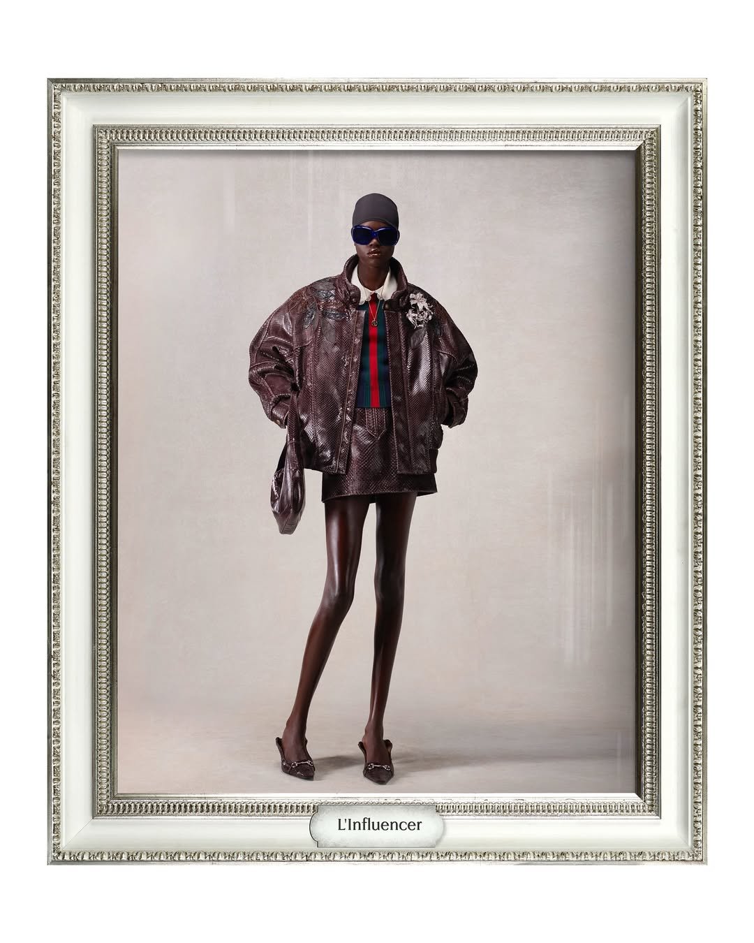 Modelo usando casaco marrom texturizado, shorts curtos e óculos escuros, em moldura sofisticada estilo Gucci de Demna.