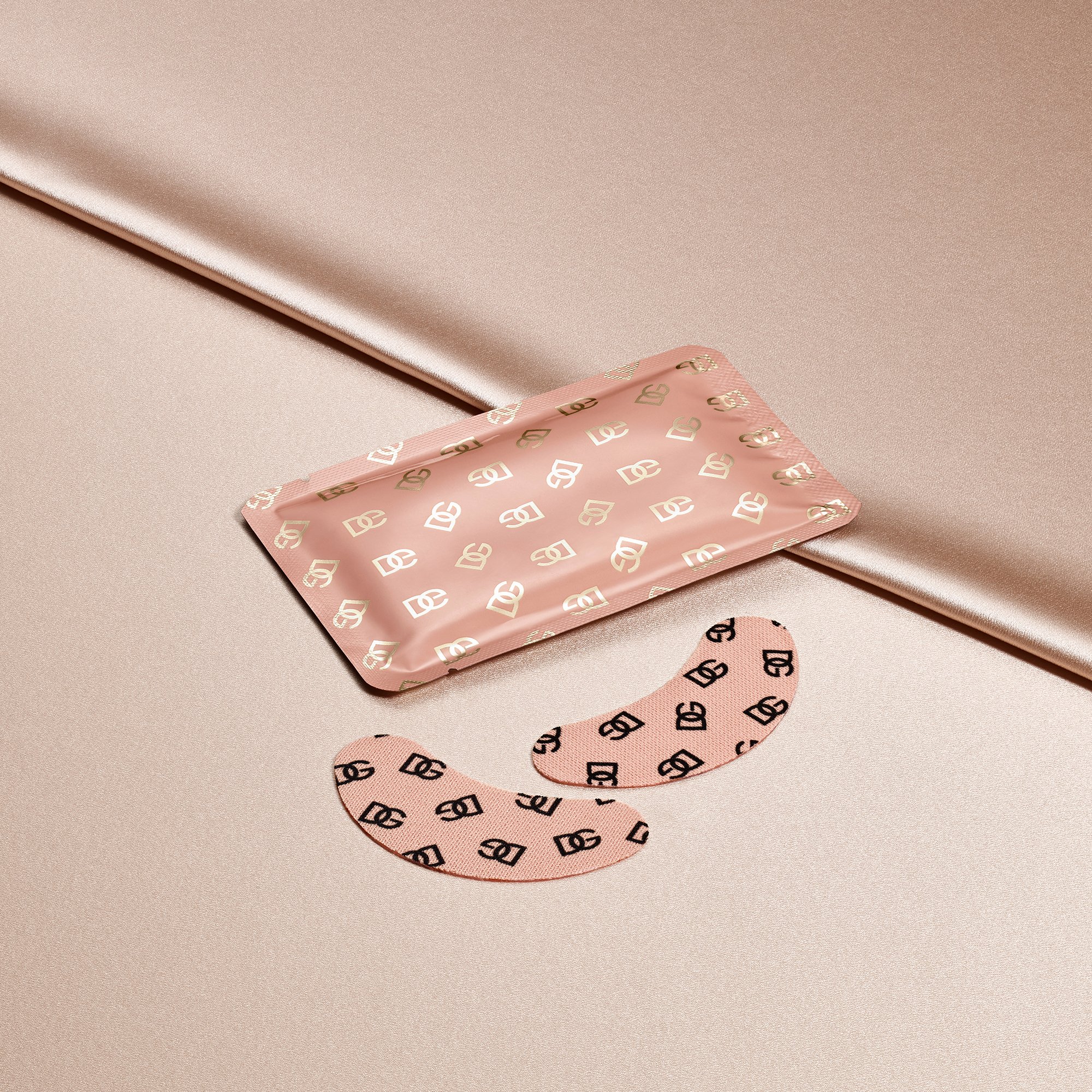 Estojo rosa com estampa de logotipos dourados ao lado de dois adesivos curvados sobre um fundo acetinado, Fresh Skin Collection.