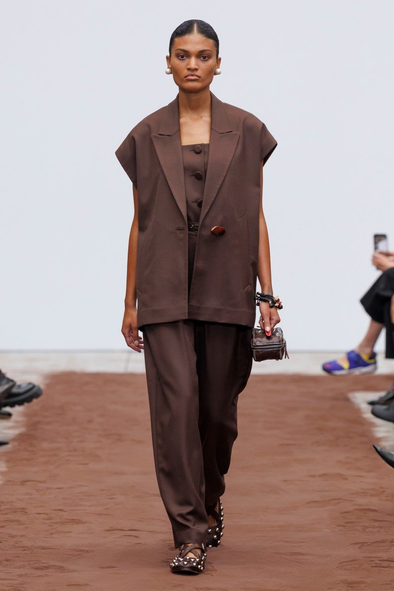 Modelo utilizando conjunto marrom em desfile da Milan Fashion Week SS26. Roupa inclui top, calça e casaco.