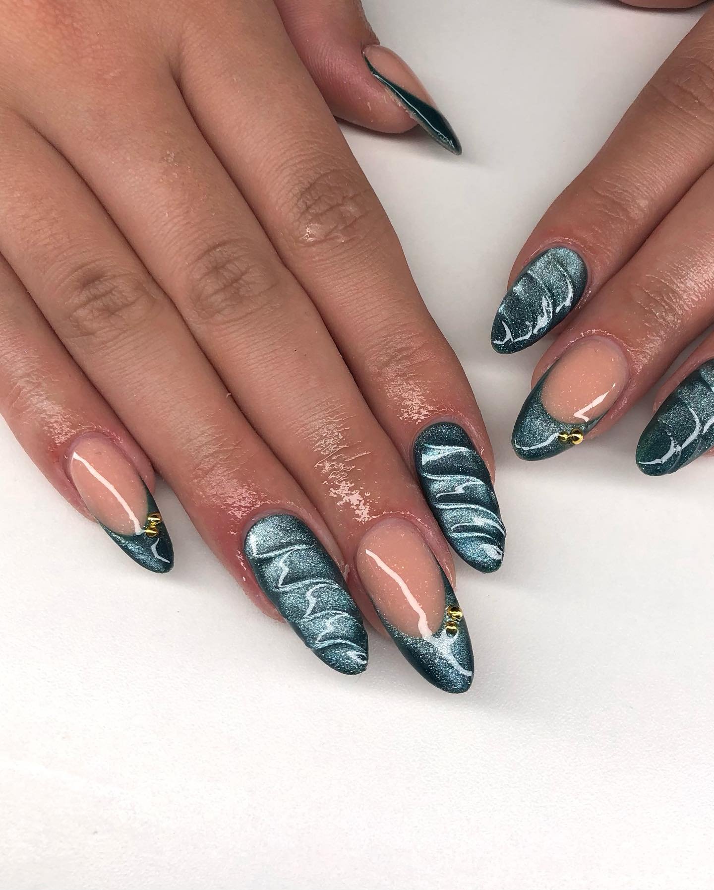 Unhas com esmalte cat eye azul, detalhes marmorizados e pequenos adornos dourados.