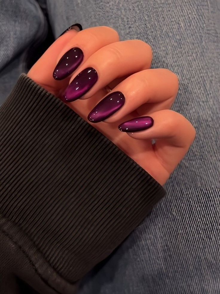 Unhas compridas pintadas com esmalte roxo brilhante, descansando sobre jeans.