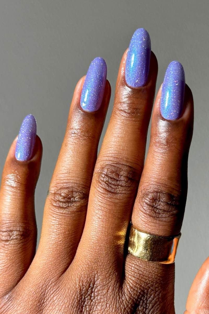Unhas com esmalte roxo cintilante e anel dourado.
