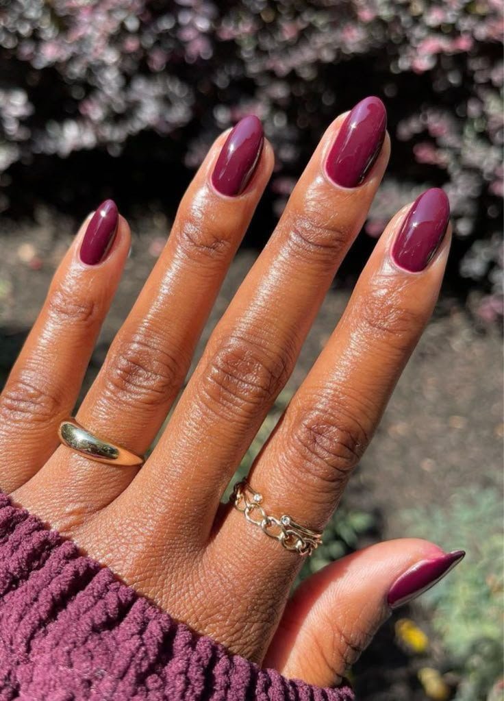 Unhas com esmalte roxo brilhante e anéis dourados em uma mão com fundo desfocado.