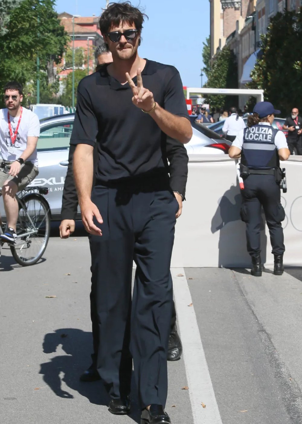 Jacob Elordi andando na rua usando uma roupa inteira preta causal enquanto faz sinal da paz.