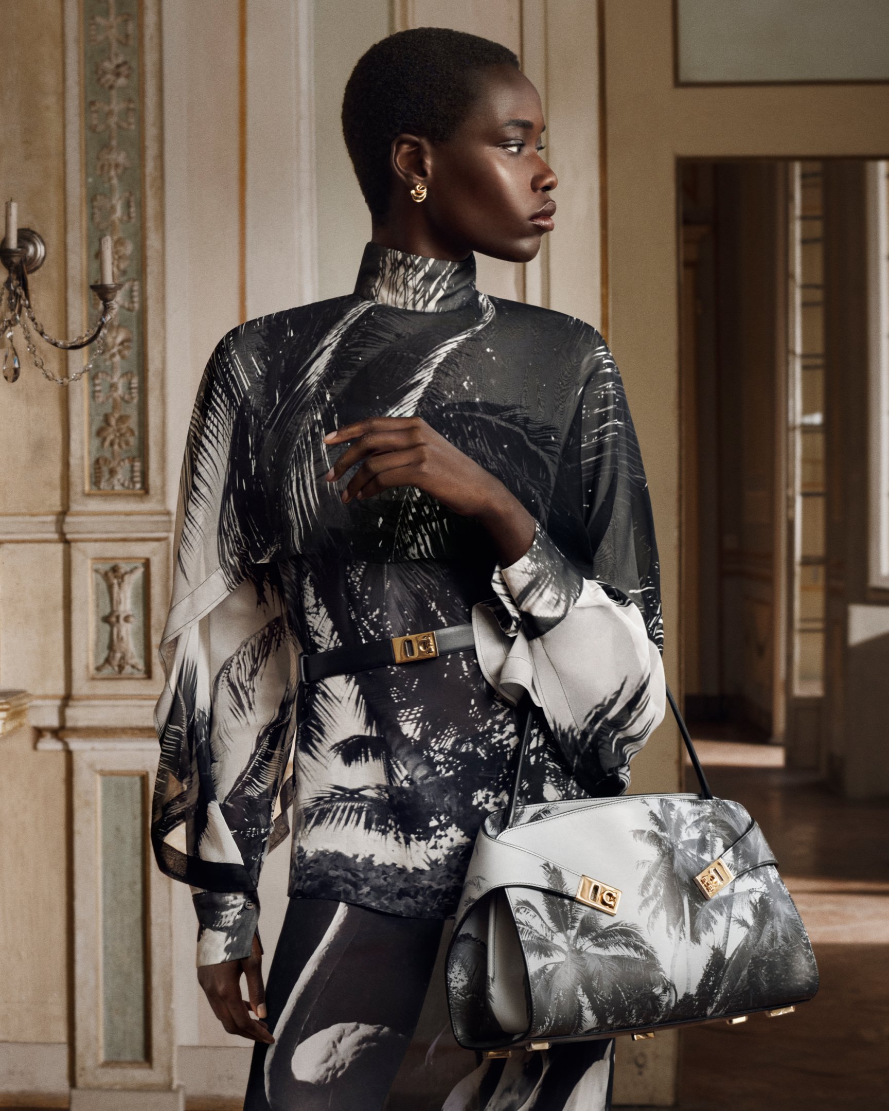 Modelo com vestido preto e branco estampado com palmeiras e bolsa Ferragamo em ambiente elegante.