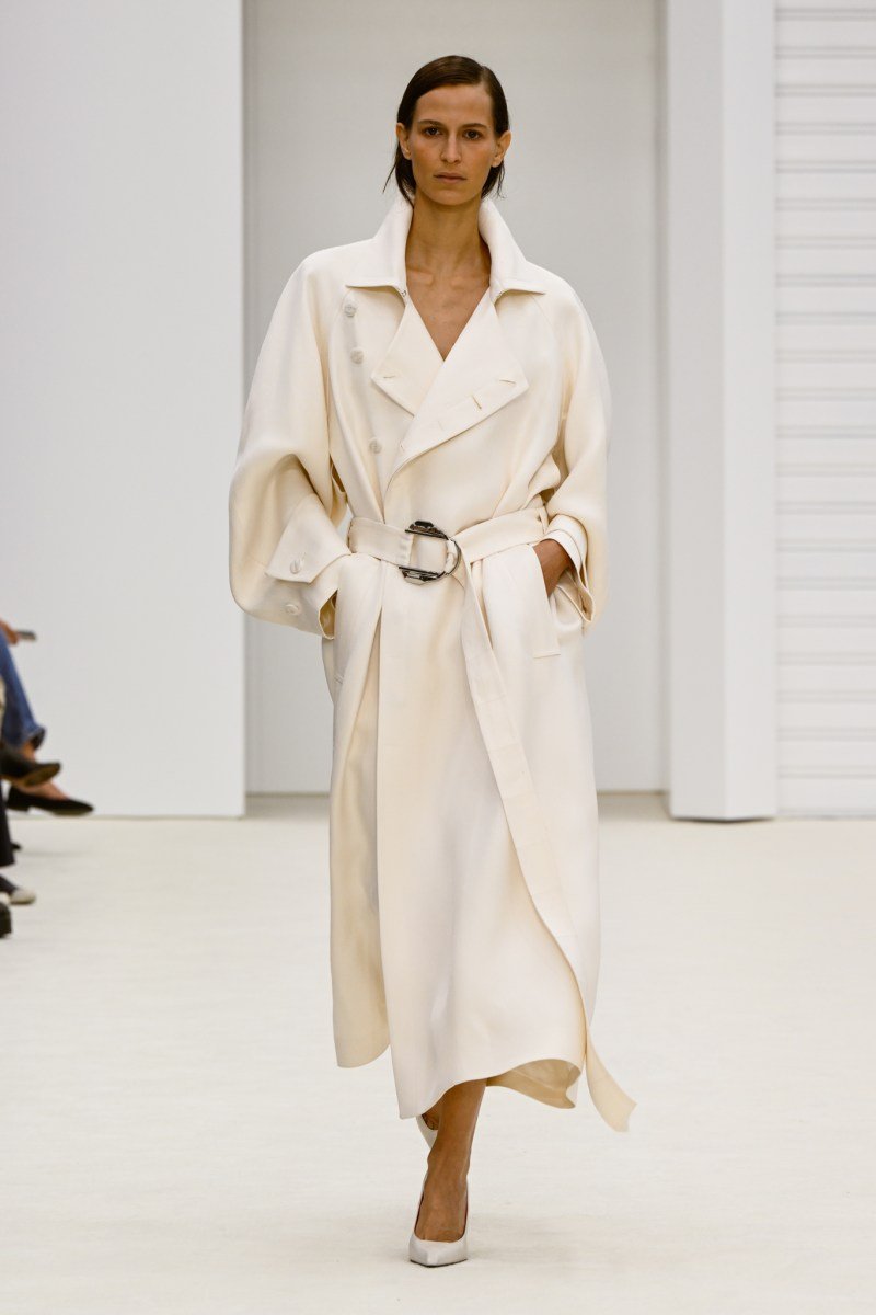 Modelo desfila em trench coat branco elegante na Milan Fashion Week SS26, com cinto, passarela minimalista.