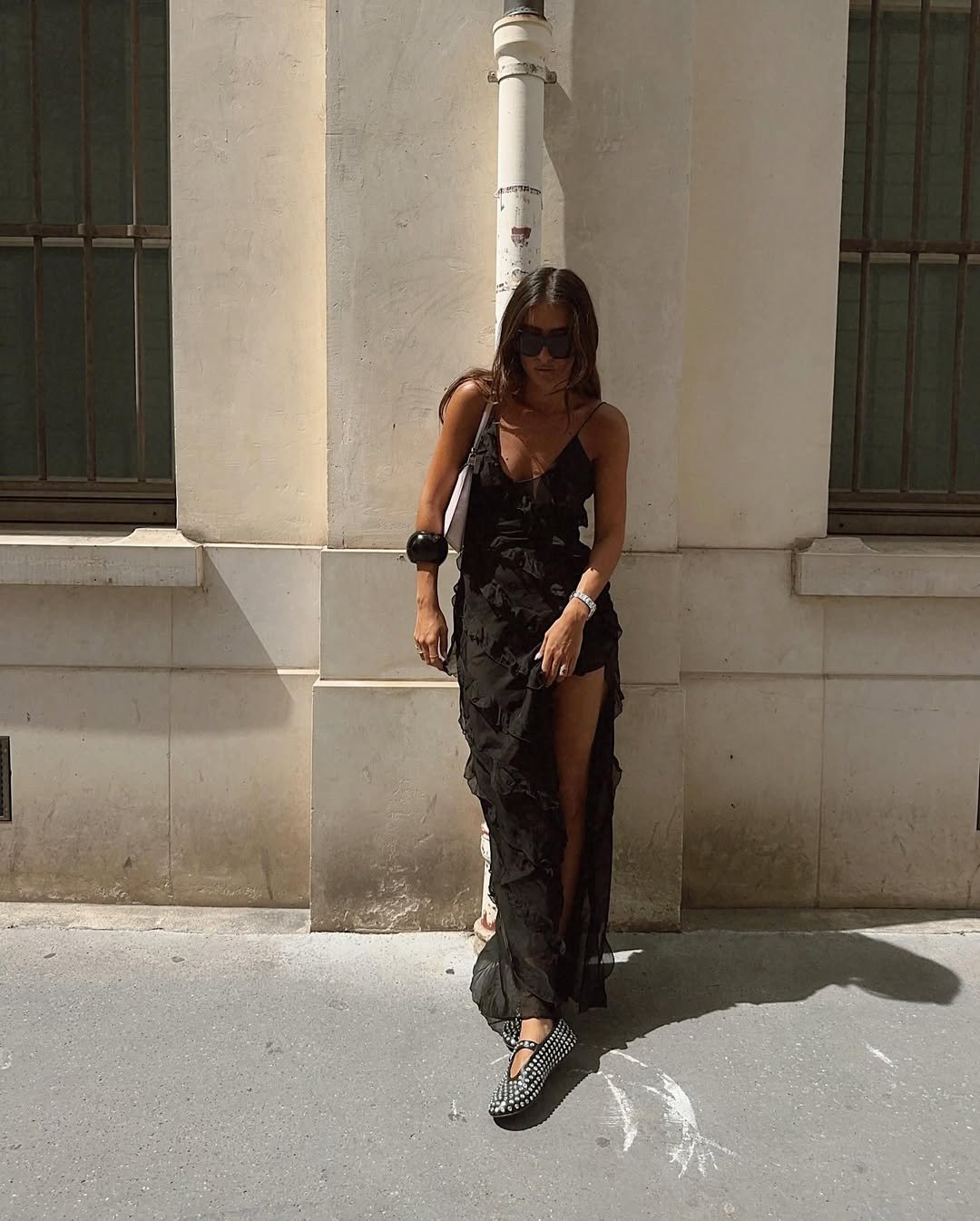 Mulher usa vestido preto longo esvoaçante e flats em padrão xadrez, destacando tendências modernas de calçados.