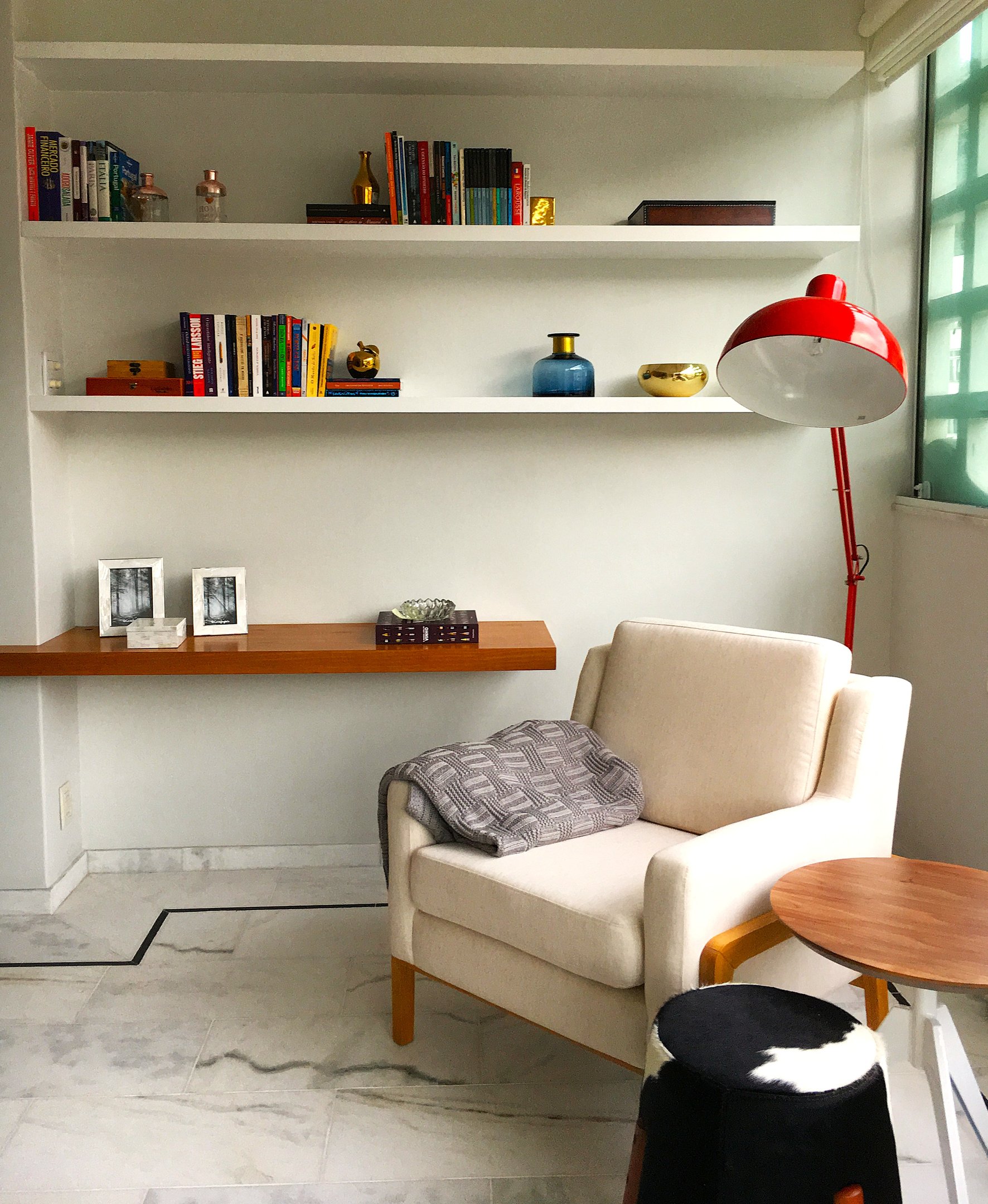 Poltrona bege ao lado de luminária vermelha, estante de livros e decorações. Ambiente elegante com dicas de decoração.
