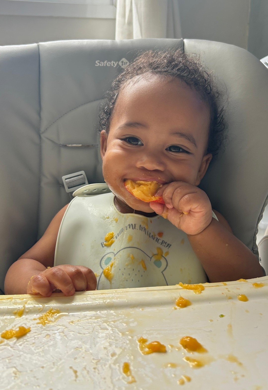 Bebê sorridente comendo fruta, explorando introdução alimentar em cadeirão.