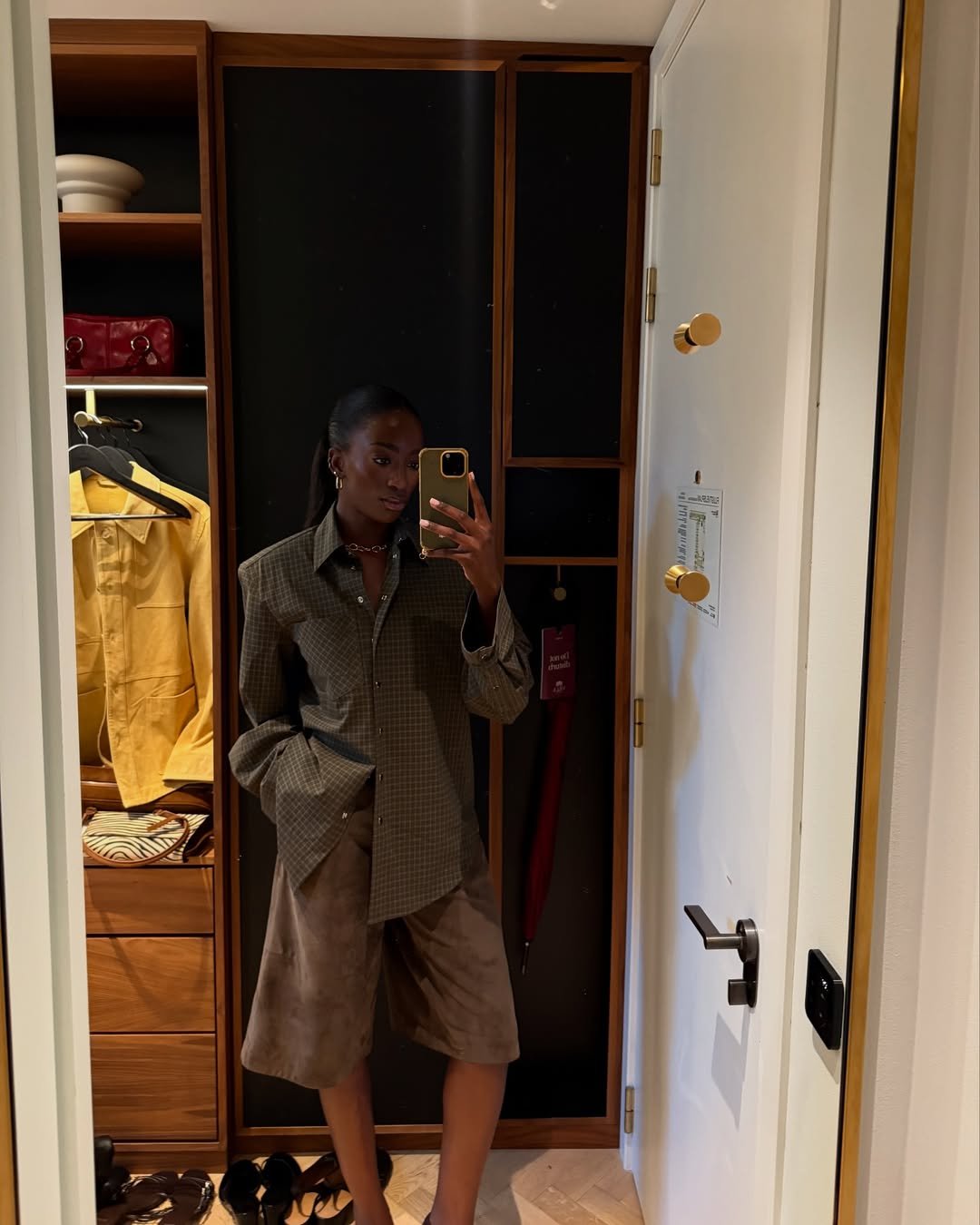 Pessoa em frente ao espelho vestindo camisa xadrez verde e shorts marrons, com guarda-roupa ao fundo.