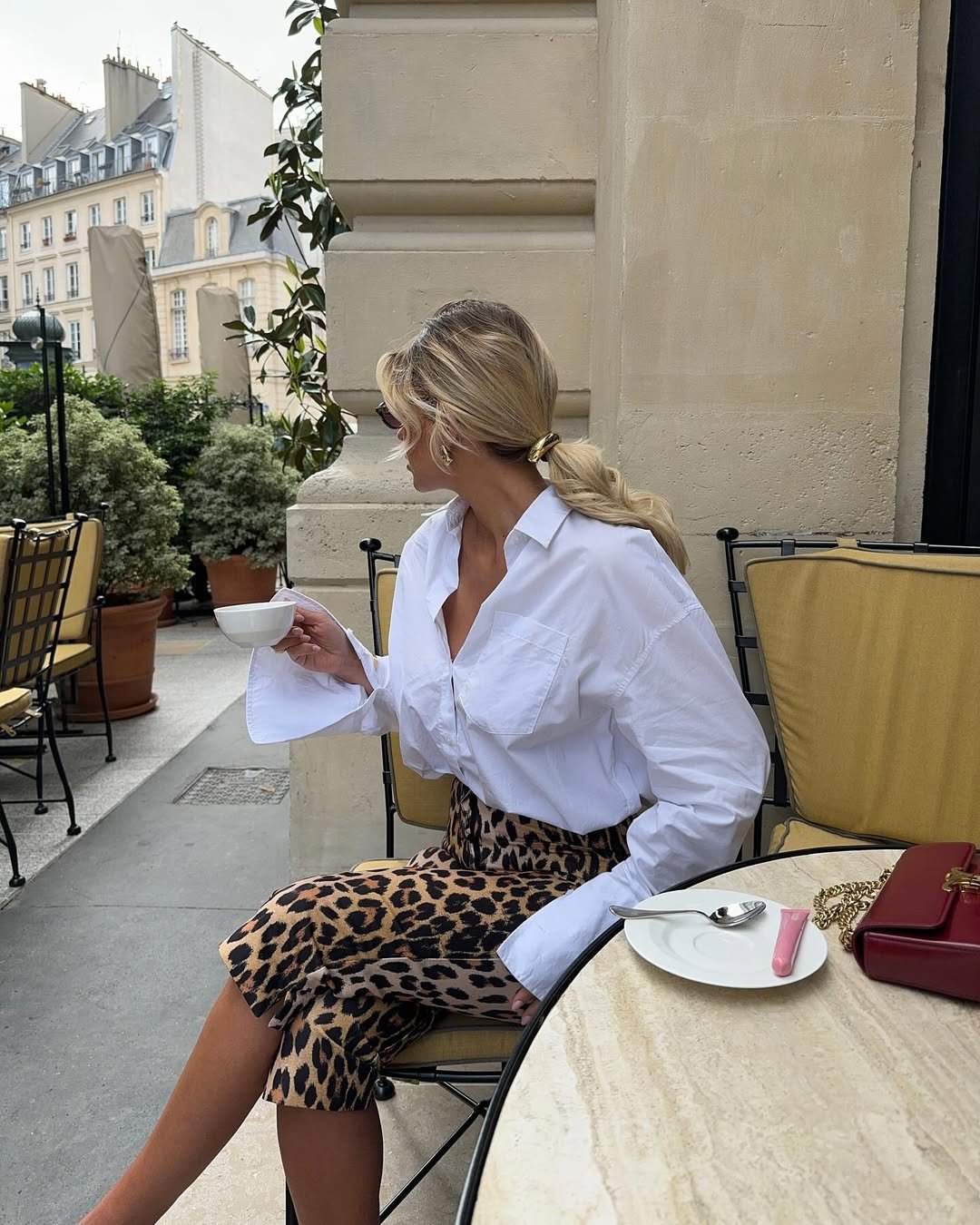 Pessoa de look com camisa branca tomando café em terraço, usando saia de estampa animal.